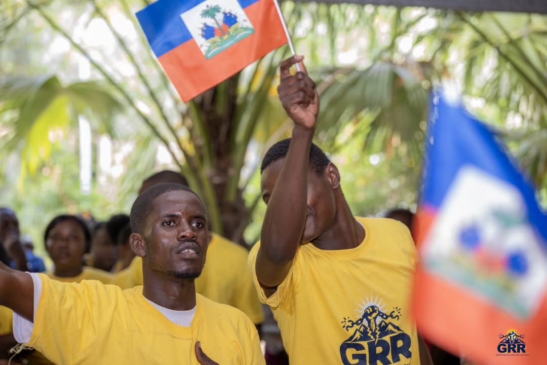 Deux jeunes membres de la GRR en t-shirt jaune du mouvement lèvent le drapeau haïtien en plein air.