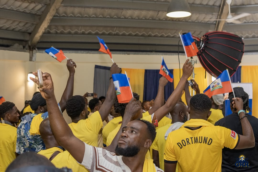 Une salle comble de membres de la GRR en t-shirt jaune brandissant des drapeaux haïtiens.